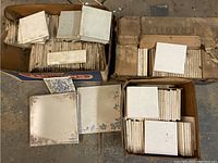 Four boxes containing assorted vintage ceramic tiles, showing various plain and decorated tiles with signs of age such as scratches and discoloration.