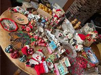 Wide view of assorted vintage Christmas items on a round wooden table. Items include nutcracker, ceramic figurines, ornaments, plates, and small holiday decorations.