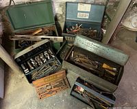 Overview of seven vintage metal and wooden toolboxes filled with old hand tools including sockets, wrenches, screwdrivers, scissors, and chisels. Signs of wear and surface rust visible.