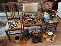 Overall view of three wooden chairs each holding vintage kitchen utensils and metal boxes set on floor with additional items.