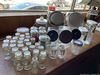 Overall display of the vintage glass jars and containers showing assortment on wooden surface by window with cars outside, highlighting quantity and variety.