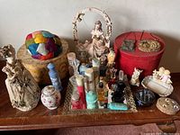 Wide view of table with vintage perfume bottles, figurines, trinket boxes, hat boxes, feather hat, antique handbags