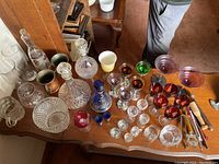 Overview of vintage assorted barware including multiple decanters, stemware in various colors, cut glass ice bucket, and bar tools on a wooden table.