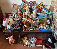 Wide view of assortment of vintage and modern toys including plush dolls, board games, and other small toys on a wooden table.
