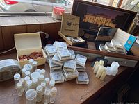 Wide angle photo showing coin holders stacked on a wood surface, metal coin box, plastic coin tubes, and some small coin boxes.
