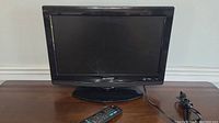 Sharp 19-inch flat screen TV standing on a wooden table, with power cord coiled beside it and remote placed in front.