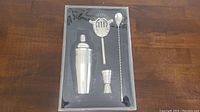 Set of four cocktail bar tools in original black packaging, showing shaker, strainer, jigger, and spoon.