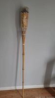 Full view of the brand new tiki torch showing natural bamboo pole and woven fuel container wrapped in plastic.