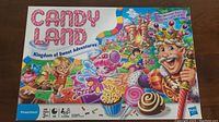 Front of Candy Land board game box showing colorful artwork with candy themed characters and treats, including a king figure, cupcakes, and whimsical candy paths.