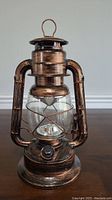 Front view of copper-finished LED lantern showing metal frame and clear glass enclosure with internal LED light source.