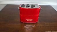Red Nostalgia Retro Series pop up hot dog maker on wooden table with metal tongs in front