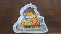Wilton Garfield cake pan featuring Garfield with closed eyes and a birthday cake with yellow icing.