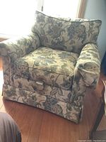Front view of a floral upholstered armchair with a loose back cushion and seat cushion, showing the skirted base and arm cover.