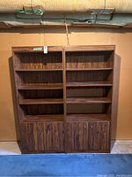 Pair of two dark woodgrain finished bookcases standing side by side. Each bookcase contains three adjustable shelves and cupboard below with doors.