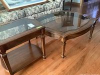Coffee table and end table placed near floral patterned couch on hardwood floor showing wood frame and glass tops.