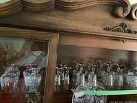 Display cabinet showing multiple crystal glasses of various types including water glasses, tumblers, and wine glasses arranged neatly for sale.