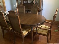 Oval wooden dining table with four matching armless upholstered chairs and two chairs with arms in a dining room setting.
