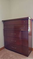 Front view of the highboy dresser showing five drawers with two different styles of gold tone knobs and visible wood grain.