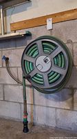 Wall-mounted hose reel with hose coiled and nozzle attached, showing overall assembly hung on wall