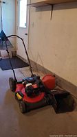 Red Craftsman push mower, grass catcher bag and red fuel can arranged on garage floor.