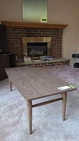 Full view of coffee table in a carpeted room, shows wood grain top and slender tapered legs.