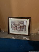 Framed print in brown frame with white matt showing a winter snow village scene with children playing.