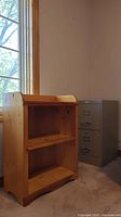 Front view of the 3-tier wooden shelf and 2-drawer metal filing cabinet in a carpeted room near window