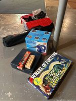 Photo showing all main items: Wheel of Fortune board game, dominoes set with wooden box, Mini Steam Zapper cleaner, black camping chair in bag, and small tote with golfing supplies including GPS device
