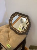 Octagonal wooden framed mirror with signs of wear placed on top of the upholstered stool.