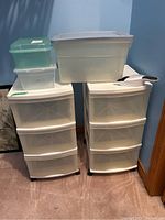 Overall shot of two Gracious Living storage drawer units on wheels with three drawers each, two clear shoe storage bins on top, one Rubbermaid tote, a whisk broom and dustpan on the right side.