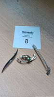 Three silver brooches including golf club pin, fish-shaped brooch with green stone, and a long curved brooch.