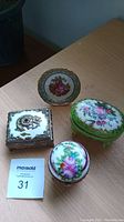 Four items on table: two floral porcelain trinket boxes, one rectangular silver-tone box with dragon design, and a decorative Limoges mini plate.