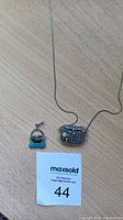 Silver necklace and turquoise purse pendant laid flat on wood surface with MaxSold tag visible.