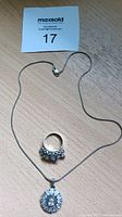 Photo showing full view of necklace chain, pendant, and ring together on a light wooden surface.