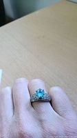 Ring being worn on hand showing overall appearance and setting with blue center stone and clear small stones on band.