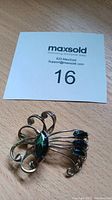 Photo of sterling silver brooch placed on wooden surface next to MaxSold lot card 16.