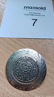 Photo of round silver brooch/pendant with detailed Aztec calendar motif in center and textured border.
