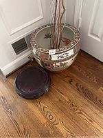 Flower pot with painted floral and scenic designs next to round wooden stand on hardwood floor
