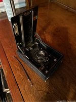 Front view of the folding camera with bellows extended and lens exposed, showing aperture and shutter settings.