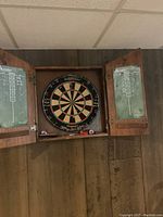 Front view of the wooden cabinet with open doors showing the Winmau dartboard and two chalk scoreboards on each door.