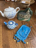 Photo of all items on wood surface: white floral teapot, green church doorstop, blue Egyptian wall hanging, small teapot candle