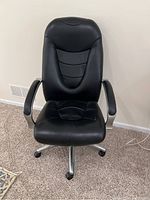 Front view of the black leather office chair showing padded seat and backrest with metallic armrest supports and caster wheels.