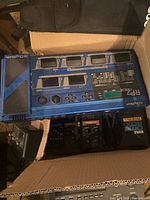 Top view of cardboard box showing blue Digitech RP7 multi-effects pedal, underneath three black pedals and Roland module edge