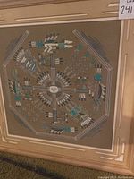 Front view of the framed Native American wall art showing the detailed symmetrical design with feathers and traditional motifs in turquoise, white, and black.