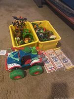 Photo of two yellow bins filled with Ninja Turtles action figures, a large Ninja Turtles-themed toy truck with red, blue, green, and white colors, and three Brain Quest card sets in front.