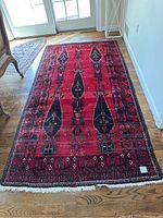Photo showing full view of rectangular runner rug with red base and black geometric designs, placed on wooden floor.