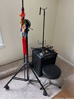 Full view of amplifier, stool, music stands, cables, drumsticks and microphone arranged together on carpeted floor.