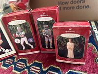 Photo of three Hallmark Keepsake boxes: Two football player ornaments and one Star Wars Boba Fett ornament. The boxes have red backgrounds with ornament images and Hallmark branding.