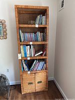 Front view of tall brown wicker bookcase with shelves holding books and bottom cabinets with metal handles.