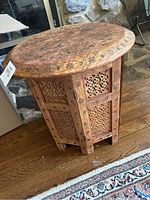 Side and top view of oval wood side table showing detailed carvings and floral motifs on surface and sides.